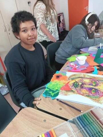 girl posing for a photograph showing her and a collage artwork she is working on