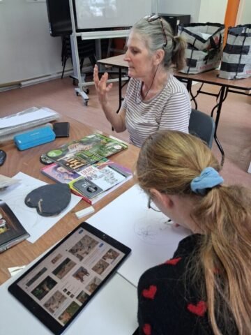 Lady teaching art to a girl who is drawing in her sketchbook