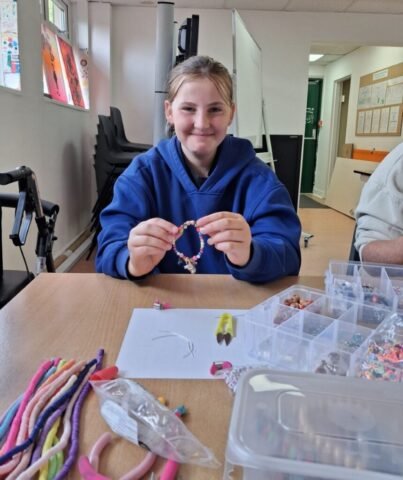 girl holding up a bracelet she has just made