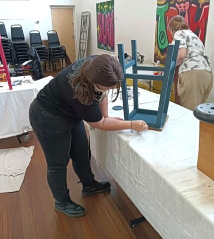 girl working on upcycling an old school stool that has been painted blue