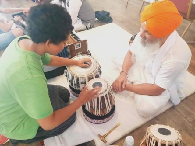 A young person with an expert Sikh musician, learning about a traditional drum